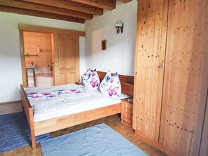A bedroom with a wooden bed, a nightstand, a wardrobe, and a door leading to another room. - Mitterbauer - Pöllmann Vacation Farm - "Seeblick Basilika" Vacation Apartment (Gaisberg)