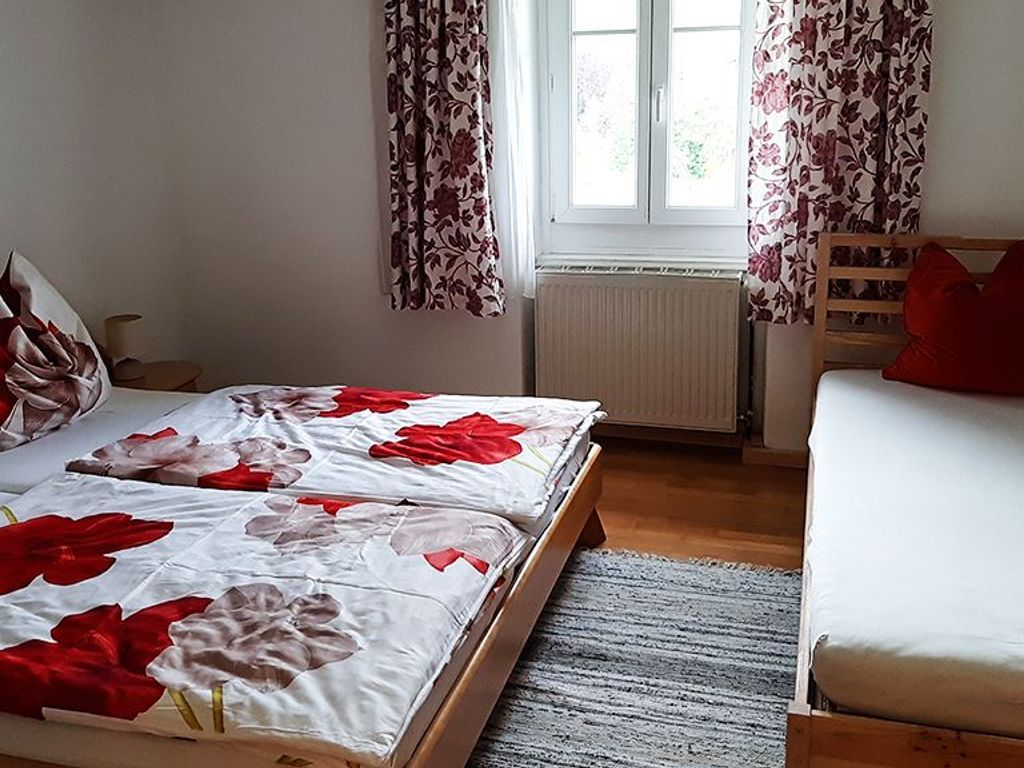 Quarto com cama, sofá, janela com cortinas e radiador.