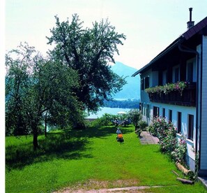 Une maison avec une pelouse, un arbre et une vue sur un lac et des montagnes.