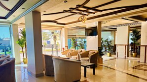Eine großzügige Lobby mit modernem Design, inklusive einer geräumigen Sitzecke mit Sofas und Sesseln, einem wandmontierten Flachbildfernseher und einem polierten Marmorboden.