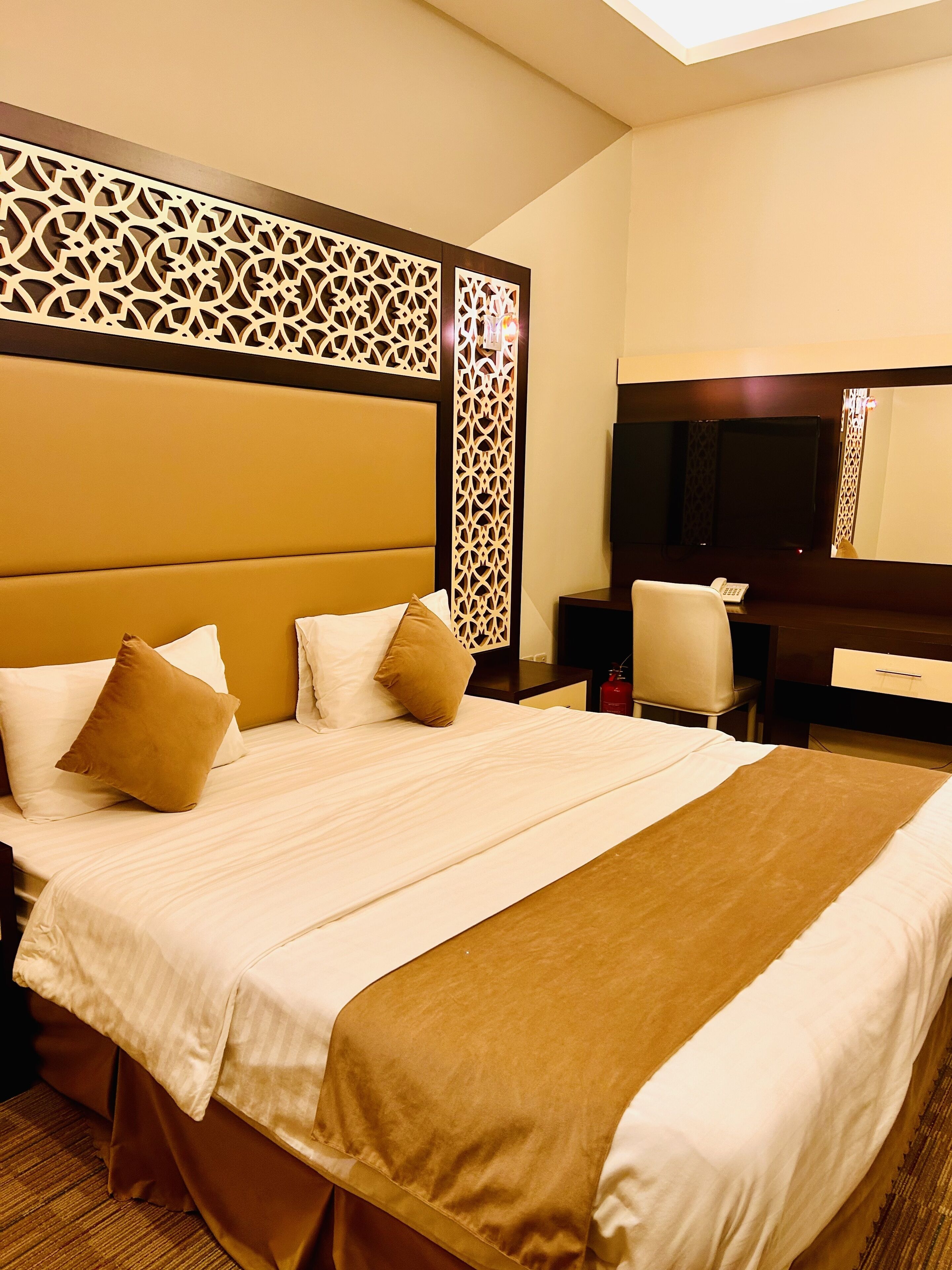 A hotel room with a large bed, a wooden headboard, a flat-screen TV, a desk, and a chair.