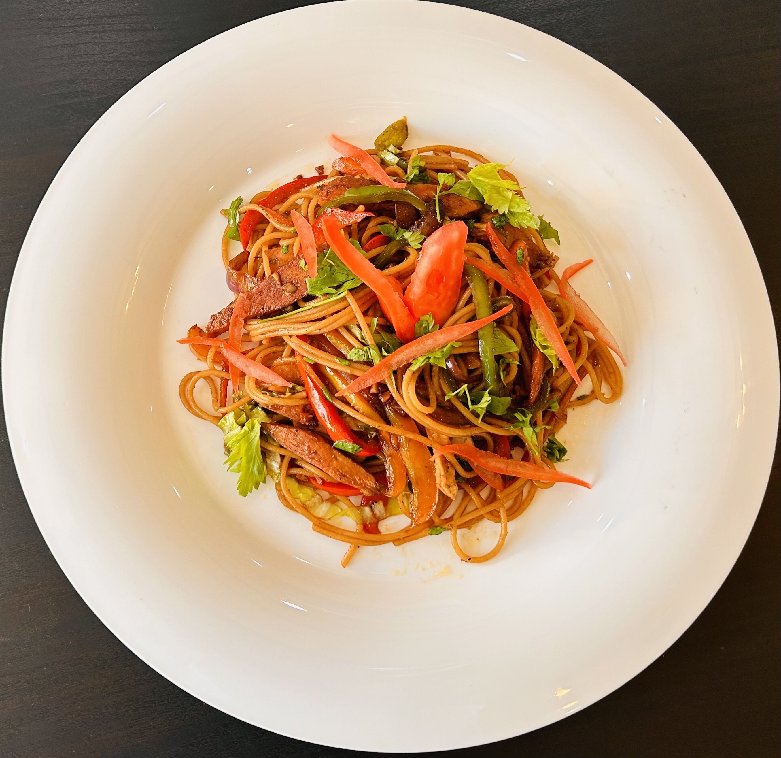 Un plato blanco con fideos, verduras y carne.