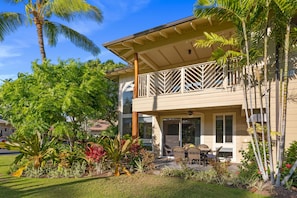 A two-story building with a balcony, surrounded by lush tropical plants and a clear blue sky.