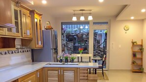 A modern kitchen with wooden cabinets, a central island, and a view of a cityscape through large windows. - Jolie House - Villa 2 Double Rooms - Great Getaway (Da Lat)