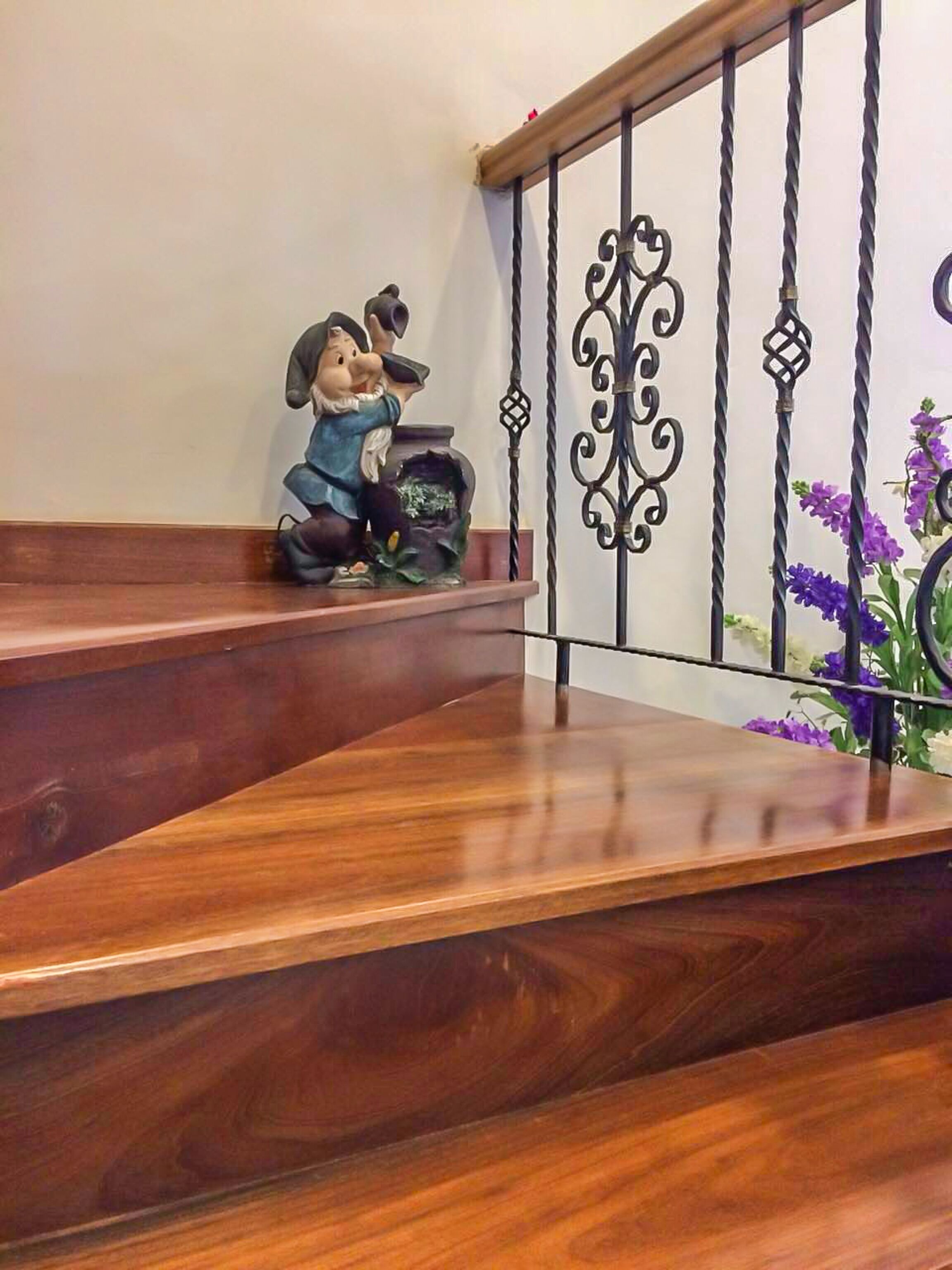Een houten trap met een decoratieve metalen leuning en een Mickey Mouse beeldje op de landingsplaats.