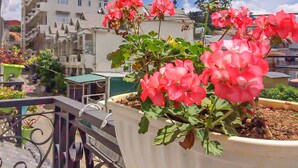 A balcony with a potted plant of pink flowers, a metal railing, and a building with multiple windows in the background. - Jolie House - Villa 2 Double Rooms - Great Getaway (Da Lat)