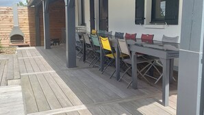 En uteplats med ett trädäck, en överbyggd sittplats med stolar och bord samt en skorsten.