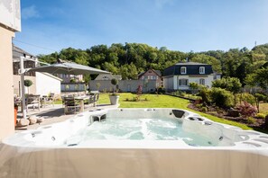 A hot tub in a backyard with a dining area and a view of houses and trees.