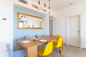 A dining area with a wooden table, yellow and blue chairs, a large mirror, and pendant lights.