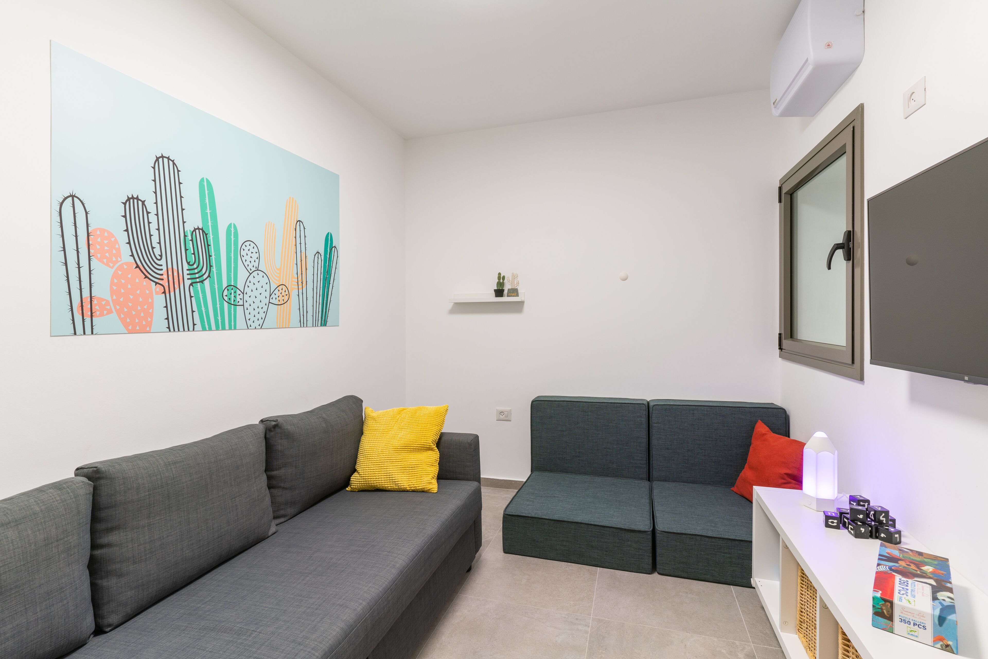 A modern living room with two grey sofas, one with a yellow pillow, and a wall art of cacti.
