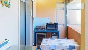 Uma pequena cozinha compacta com micro-ondas, torradeira e uma mesa com cadeiras.