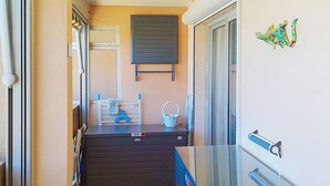 Um corredor estreito com piso de azulejos, um armário azul, uma estante de metal com uma cesta, e uma porta com maçaneta.