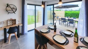 Comedor con una mesa dispuesta para cuatro, una botella de vino y vista a un jardín a través de amplios ventanales.