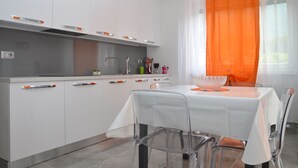 Eine moderne Küche mit weißen Schränken, einer Edelstahl Arbeitsplatte und einem Essbereich mit weißem Tisch und Stühlen.
