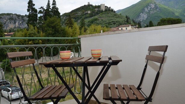 Ein Balkon mit Holzkstühlen und einem Tisch, mit Blick auf eine Berglandschaft mit einem Schloss.