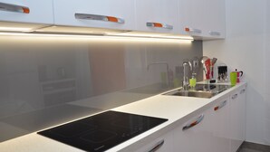 Eine moderne Küche mit weißen Schränken, einer schwarzen Induktionskochplatte und Edelstahlgeräten.