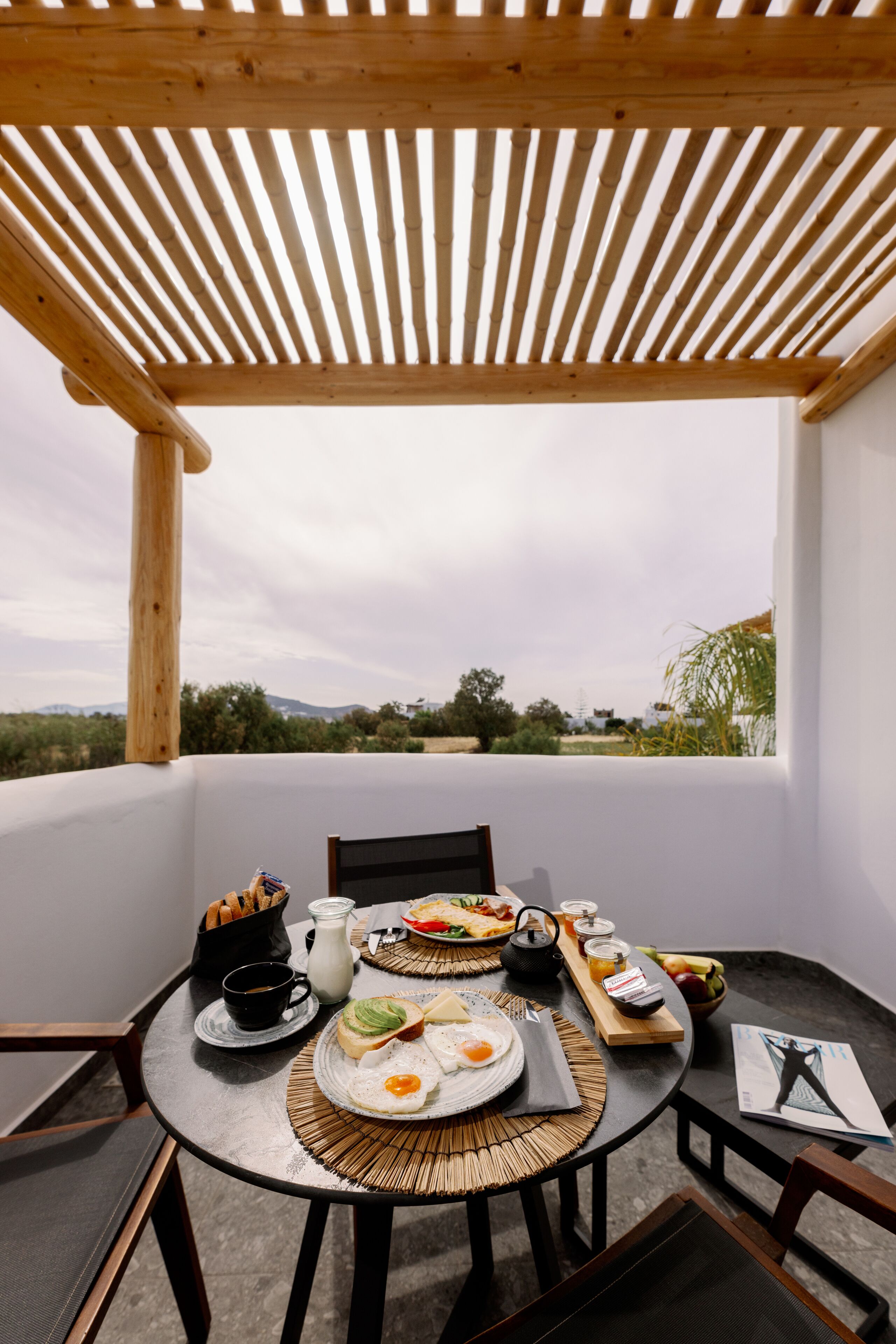 Una mesa de comedor con alimentos para el desayuno, una revista y vistas al campo.