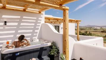 A rooftop terrace with a hot tub, wooden pergola, and a table with chairs and a fruit basket.