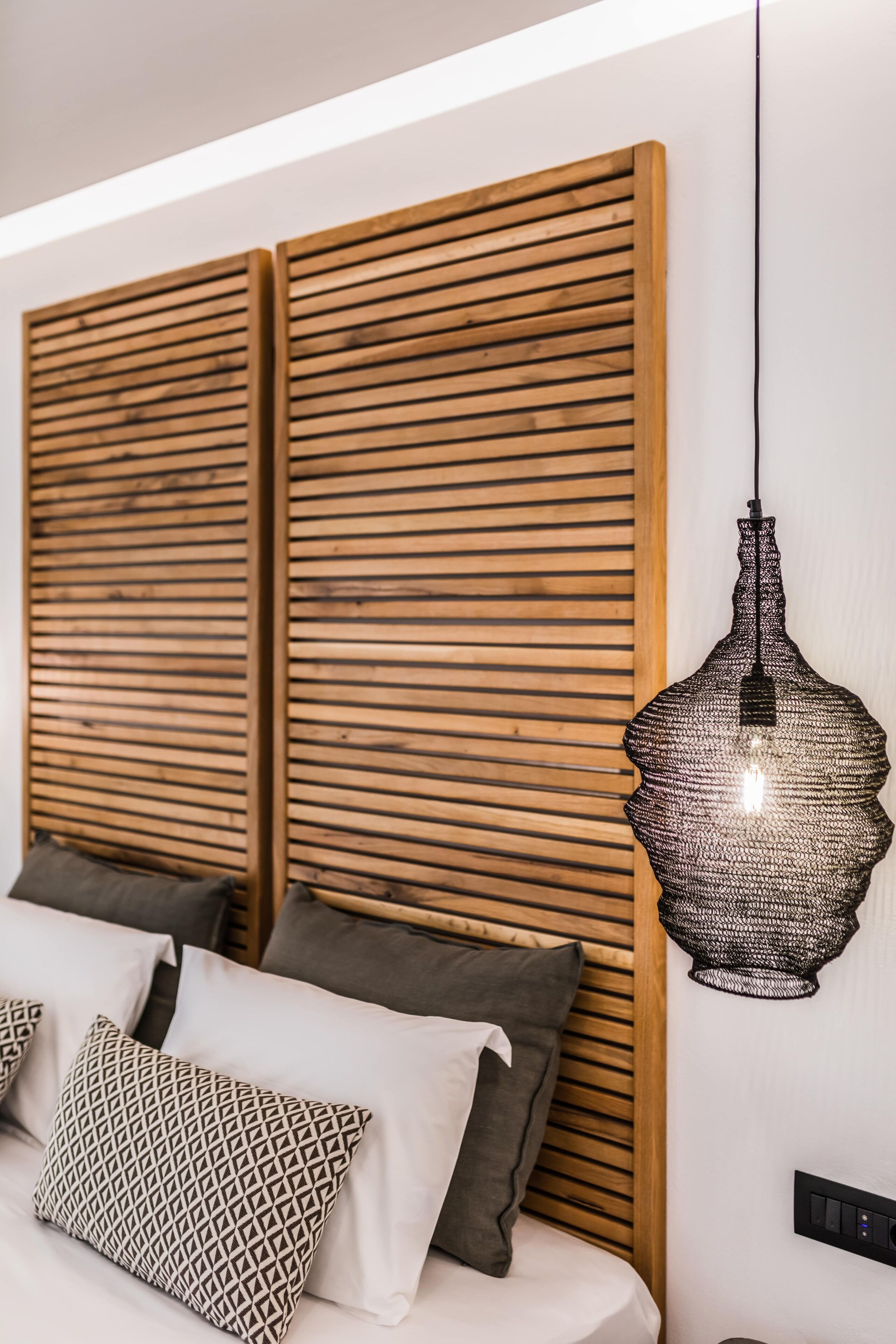 A modern bedroom with a wooden headboard, a hanging pendant light, and patterned pillows.