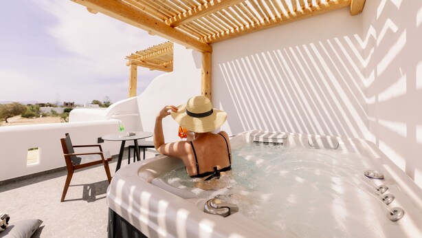 Una persona en un jacuzzi bajo una pérgola de madera en una azotea con vistas al paisaje.