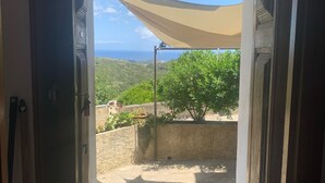 Une porte ouverte donnant sur un patio d’où l’on peut admirer la mer et la verdure.