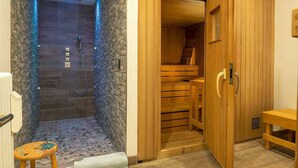 A sauna room with a wooden bench, a small stool, and a shower area with a hose. - Appartamento Livigno (Livigno)