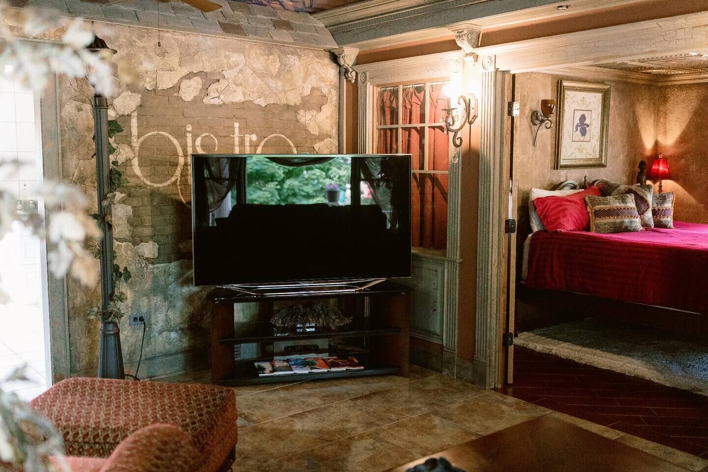 A cozy living room with a television, a fireplace, and a bed with red bedding.