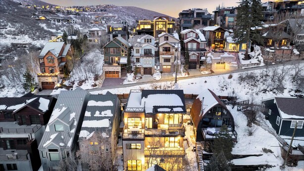 A snow-covered residential area with various houses and buildings, including a prominent house with a large balcony and multiple windows. - The Ontario | 5BR Epic Views, Heart of Park City (Park City)