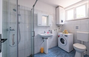 Ein Badezimmer mit Duschkabine, Waschbecken, Waschmaschine und Toilette.