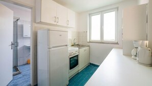 Cocina compacta con armarios blancos, horno integrado, lavabo y ventana que proporciona luz natural.