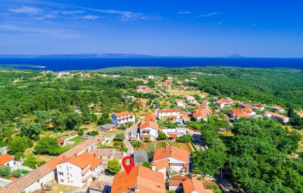 Luftaufnahme eines Küstdorfes mit Häusern, einem roten Markierungspunkt und Blick auf das Meer und die dahinterliegenden Hügel.