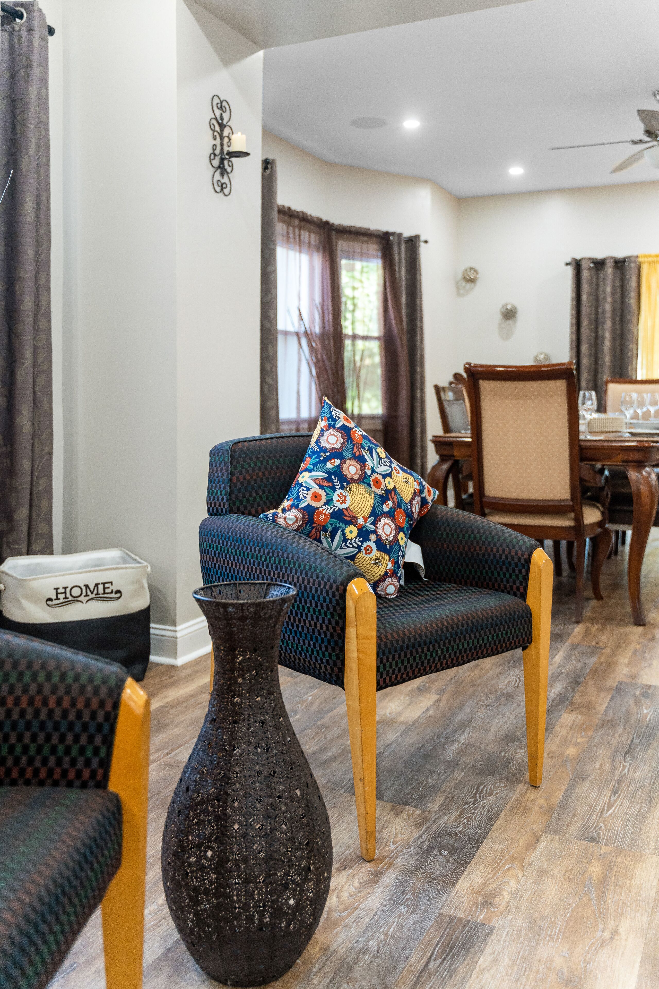 A living room with a sofa, a decorative vase, a dining table with chairs, and a ceiling fan.