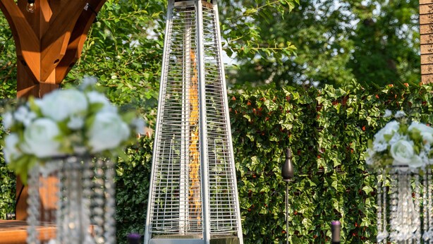 Un espacio de comedor al aire libre con una estructura de pérgola, un farol de metal alto y mesas dispuestas para una comida.