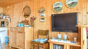 A wooden cabin interior with a kitchen area, a dining table, a television, and various decorative items on the walls.