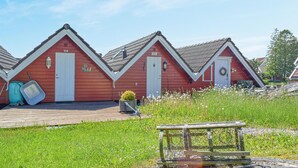 A row of red wooden cabins with white doors, numbered 324 and 326, set in a grassy field with a wooden bench in the foreground.