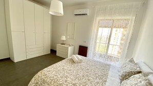 Un dormitorio con cama, cómoda, armario, ventana con cortinas y aire acondicionado.