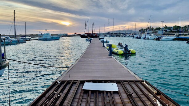 Un muelle de madera que se adentra en un puerto deportivo con varias embarcaciones amarradas.