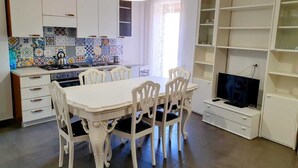 Una cocina compacta con armarios blancos, salpicadero de azulejos y una zona de comedor con sillas y una mesa blancos.