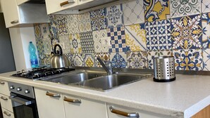 Una cocina con armarios blancos, un lavamanos de acero inoxidable, un hervidor y un rallador.
