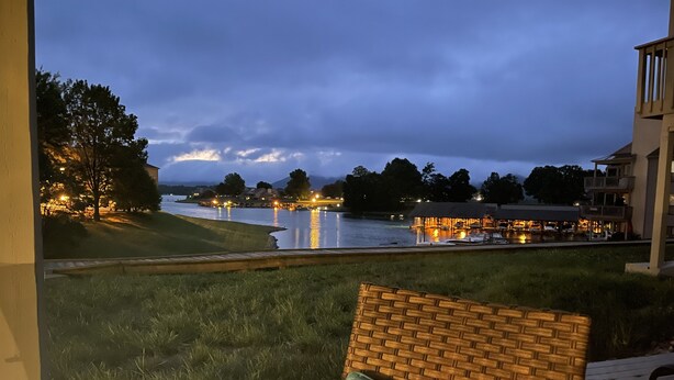 Vista desde un balcón sobre un lago, con un restaurante y edificios al fondo.
