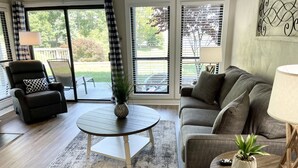 Una sala de estar con un sillón reclinable negro, un sofá gris, una mesa de centro redonda y una alfombra estampada.