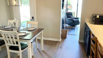 A dining area with a table set for four, a chair, and a hanging light fixture.