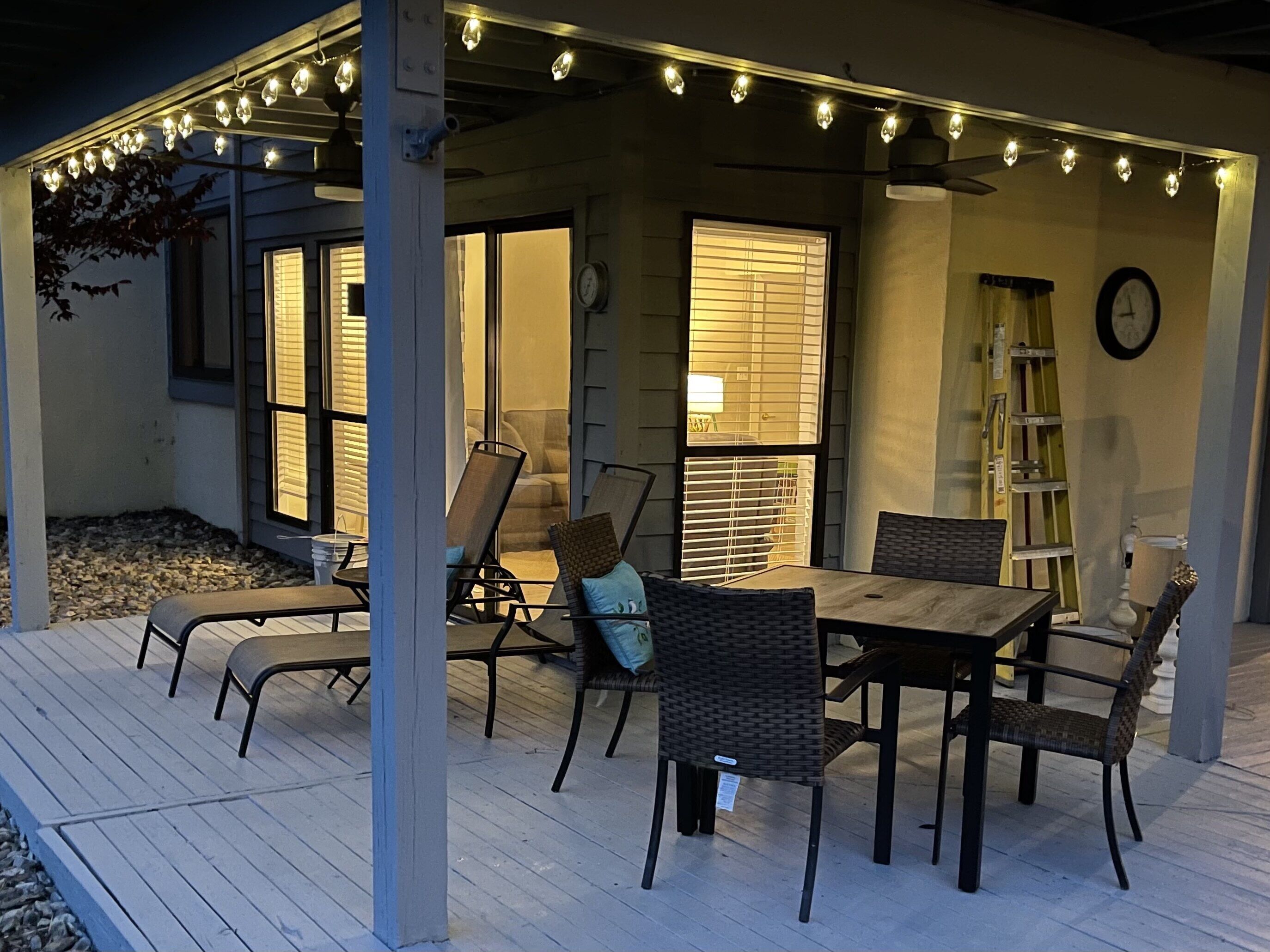 An outdoor patio with a wooden deck, wicker furniture, and string lights.