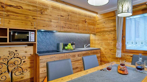 A modern kitchen with wooden cabinetry, a built-in microwave, and a dining area with a table set for two. - Aparment for holiday  (Livigno)