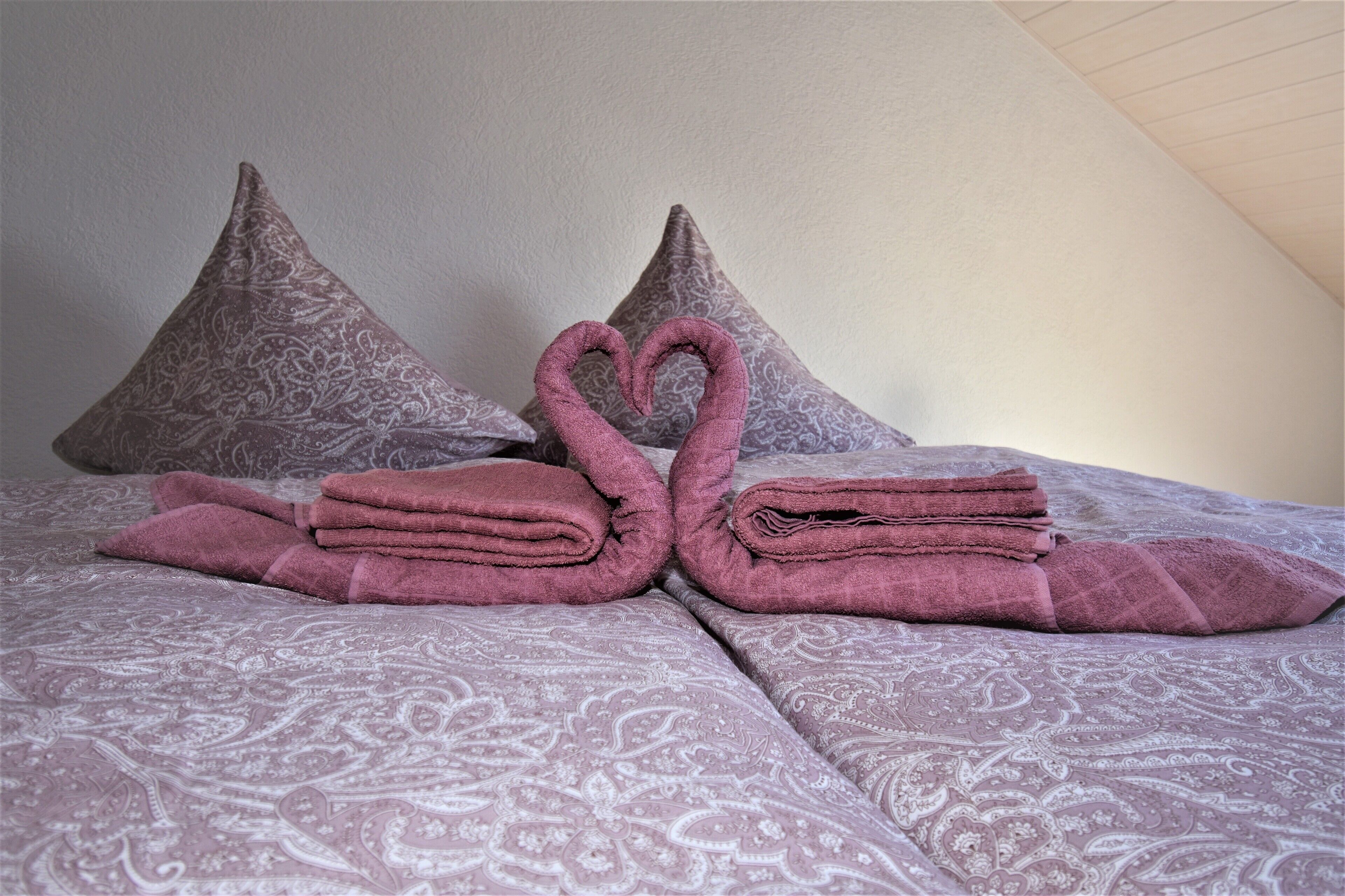 Un lit avec une couvre-lit à motifs, deux oreillers et des serviettes pliées disposées en forme de cygne.