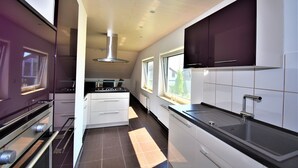Een moderne keuken met een fornuis, oven en spoelbak. Uitsluitend kasten en een raam zorgen voor natuurlijk licht.