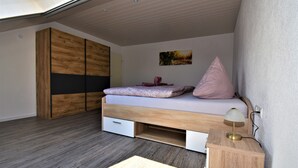 Een slaapkamer met een bed, nachtkastje, lamp, kledingkast en een schilderij aan de muur.