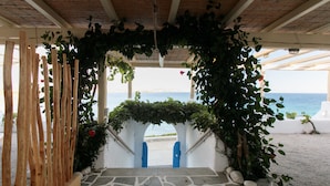 A stone-tiled entrance with a wooden fence and blue gates leading to a beach view. - Avali Deluxe Suite II (Naxos)