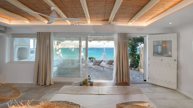 A modern room with a large sliding glass door leading to a balcony with a view of the sea. - Avali Deluxe Suite II (Naxos)
