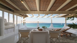 A covered outdoor dining area with a table set for two, overlooking the sea. - Avali Deluxe Suite II (Naxos)